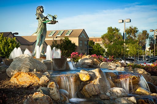 Statue beside cascading water fountain under clear blue sky.